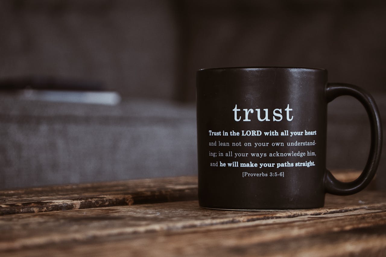 Black ceramic mug with white religious text from Holy Bible placed on shabby wooden surface in room